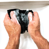 man hands washing a black facial bamboo washcloth in the sink with soap
