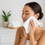Woman cleaning her face with a white towel in a serene setting