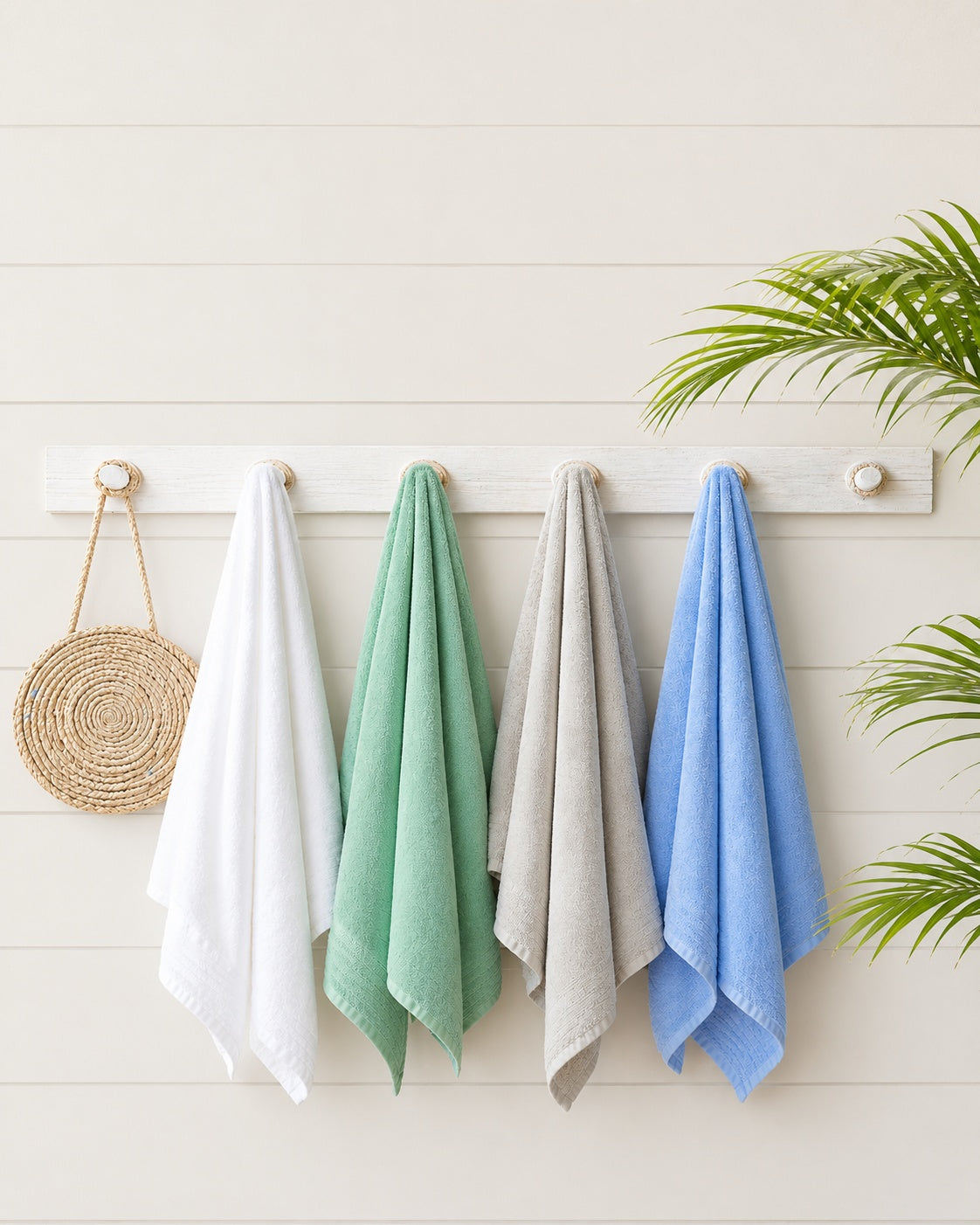 Four colorful towels hanging on a rack against a light wooden wall with a plant in the corner.