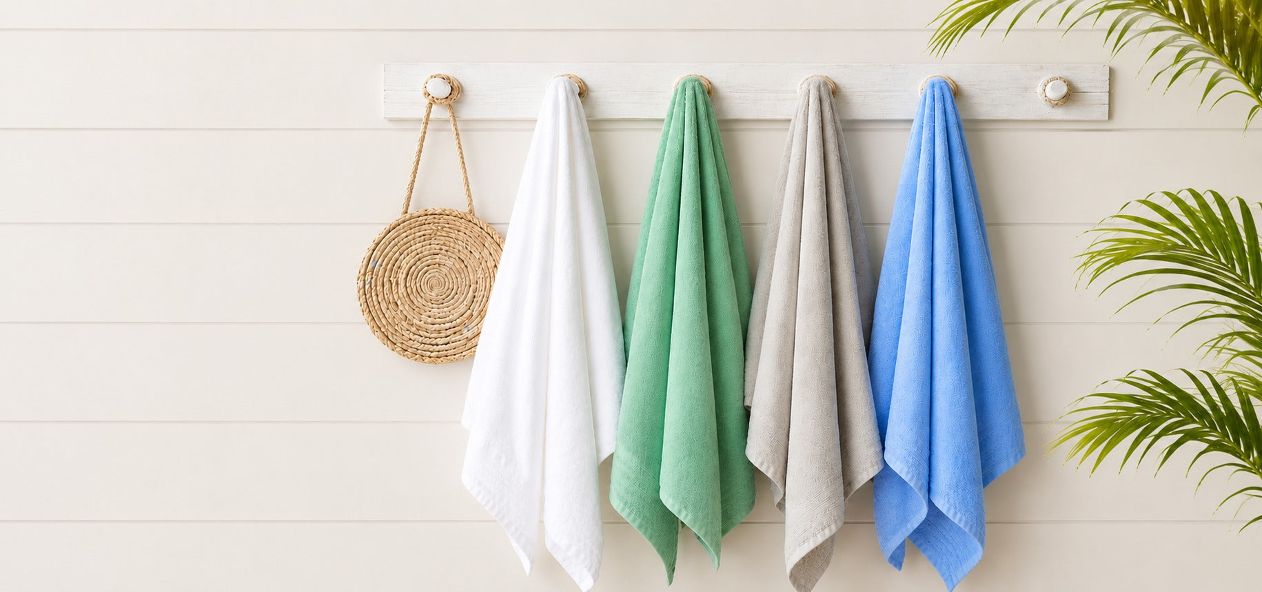 Four colorful towels hanging on a rack against a light wooden wall with a plant in the corner.