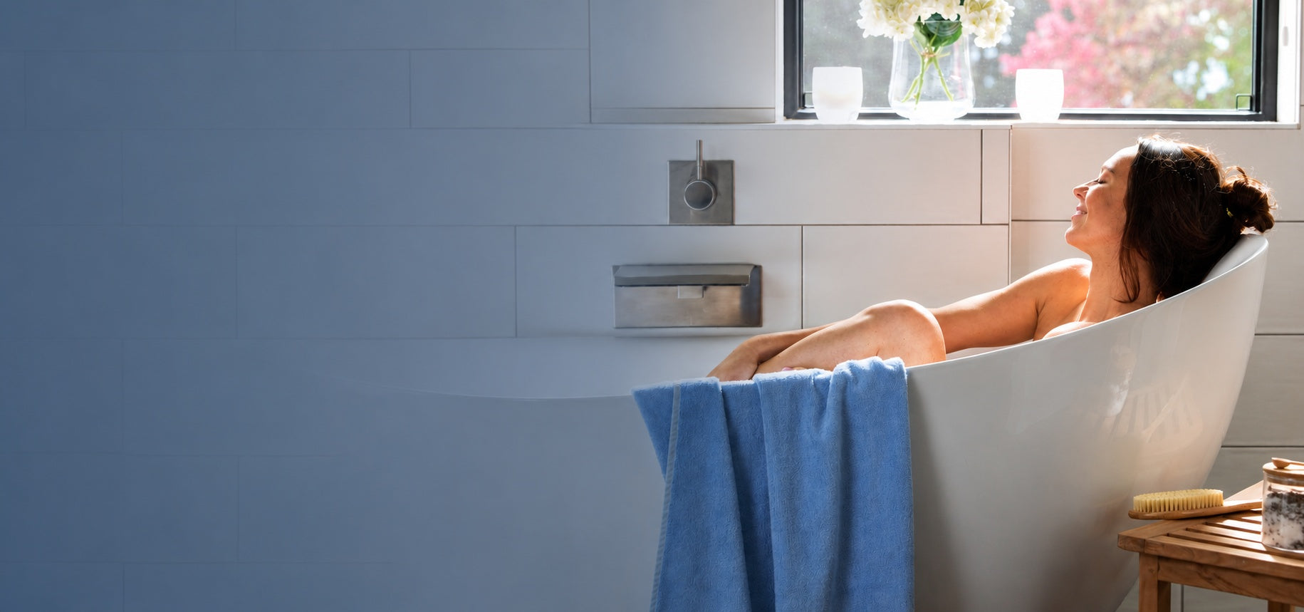 woman smiling in beautiful bathtub with ocean blue bamboo towels draped over tub