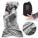 woman sleeping under a gray bamboo sleeping bag with a black carrying bag labeled 'Bedvoyage' on a white background.
