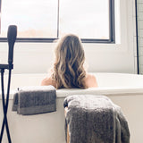 woman in bathtub with charcoal melange bamboo bath sheet and hand towels near her