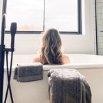 Person sitting in a bathtub with towels draped over the sides, looking out a window.