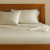 Beige bamboo bed sheets and pillows on a wooden bed with a wooden headboard.