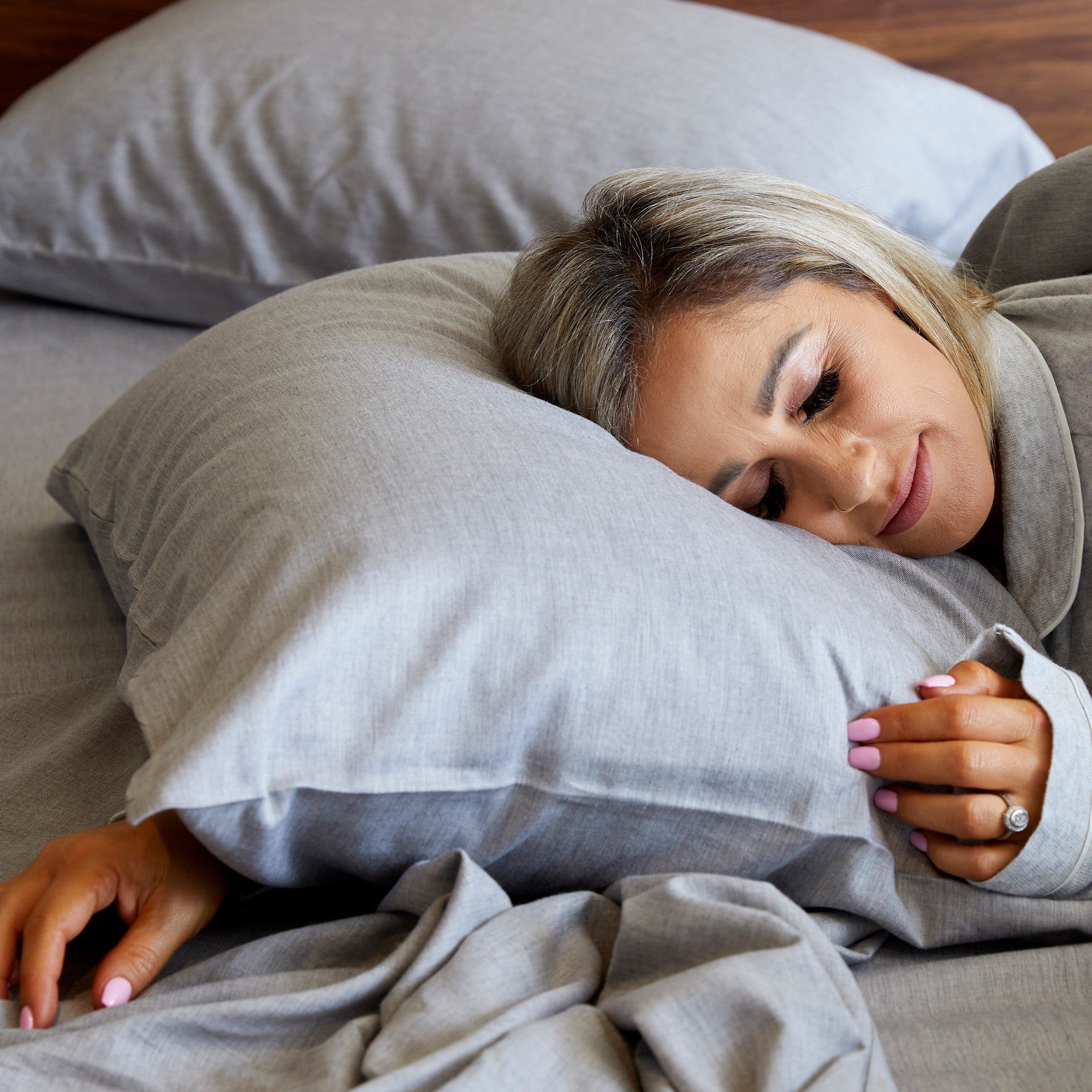 Woman lying on a gray pillow in bed, wearing a gray sweatshirt.
