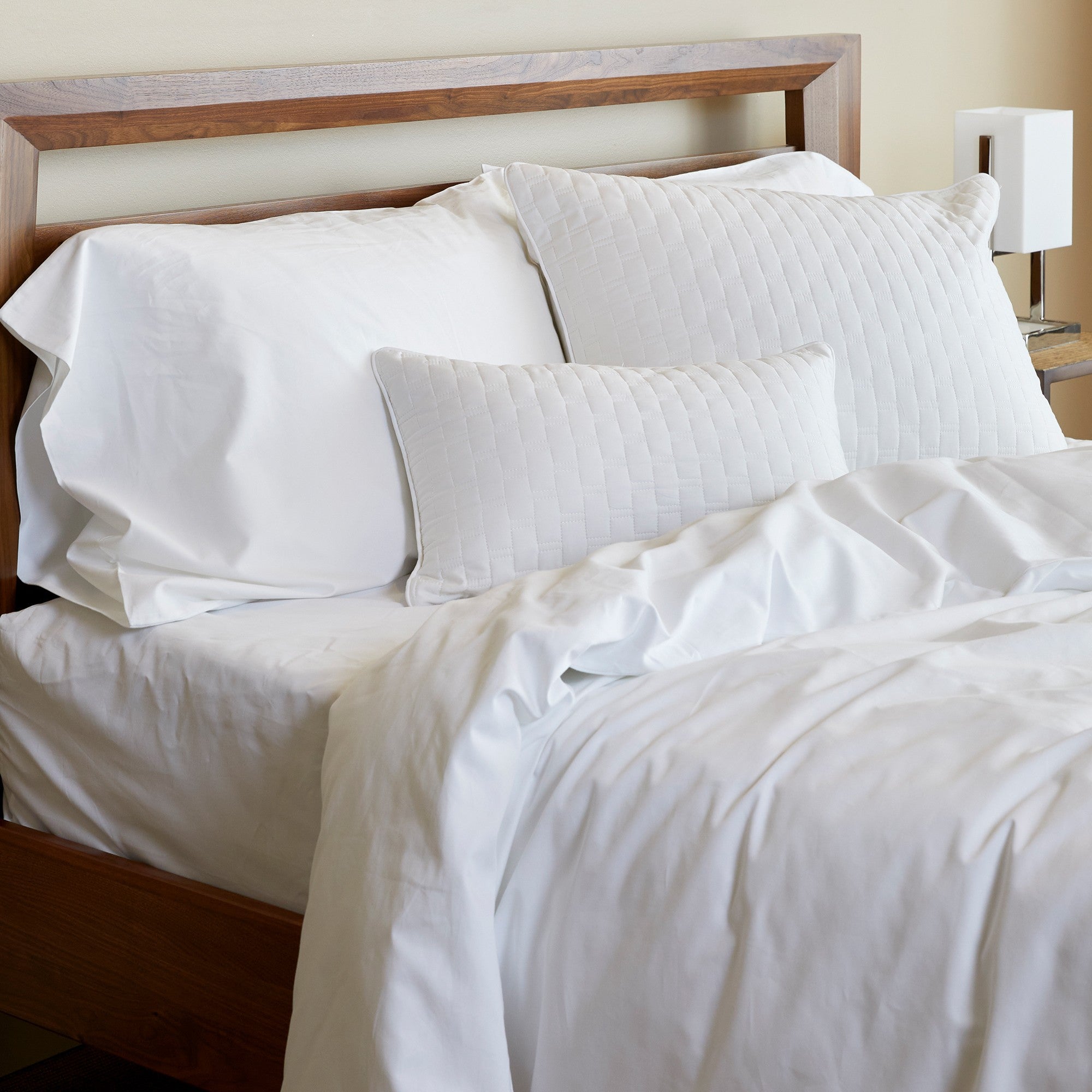 white bamboo comforter duvet cover and pillows with quilting on bed with wood headboard and small white lamp and tan walls