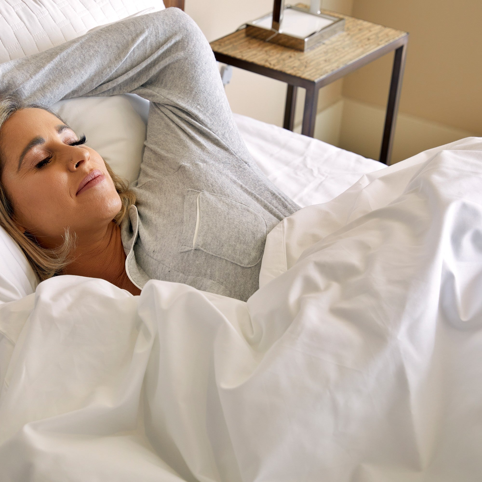 woman in gray pajamas sleeping in bed on white bamboo sheets wood side table and lamp