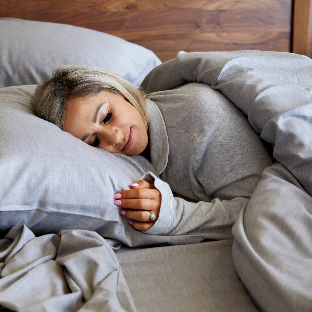 woman sleeping in silver gray bamboo sheets in gray pajamas and wood headboard