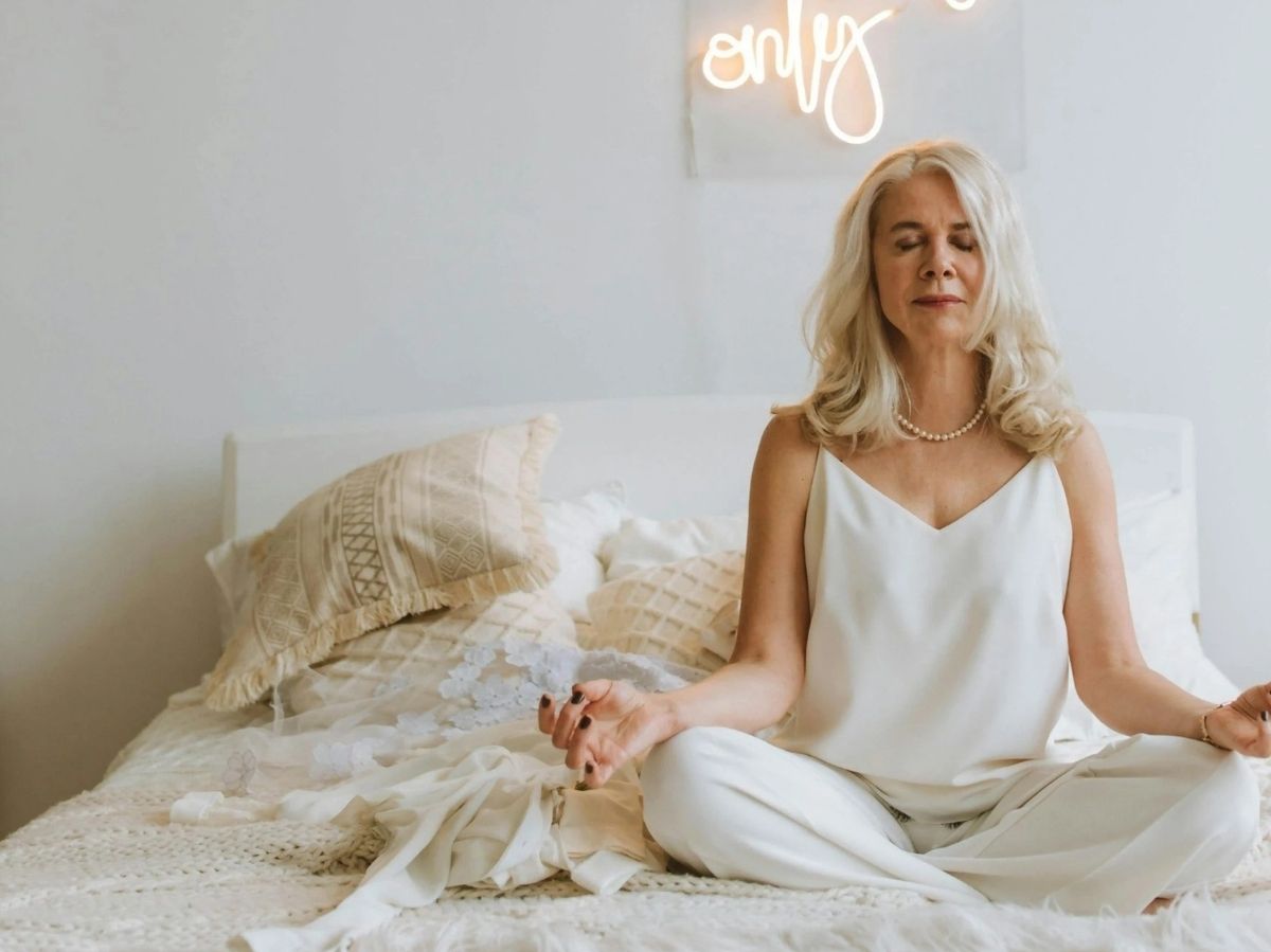 Woman in a white dress sitting on a bed with a 'only' neon sign in the background