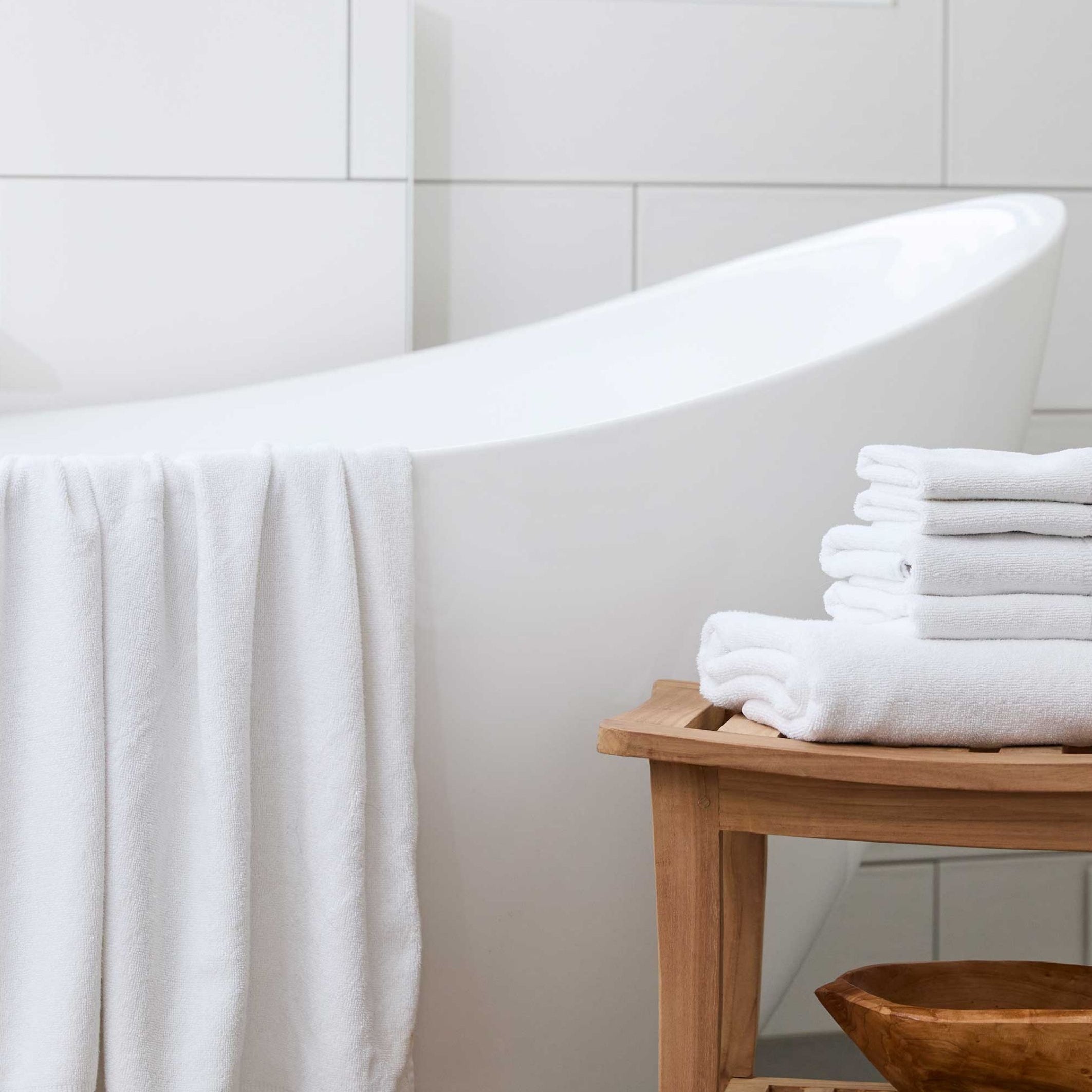 white bamboo towel draped over white tub and 5 gray towels stacked on bamboo stool in pretty bathroom 