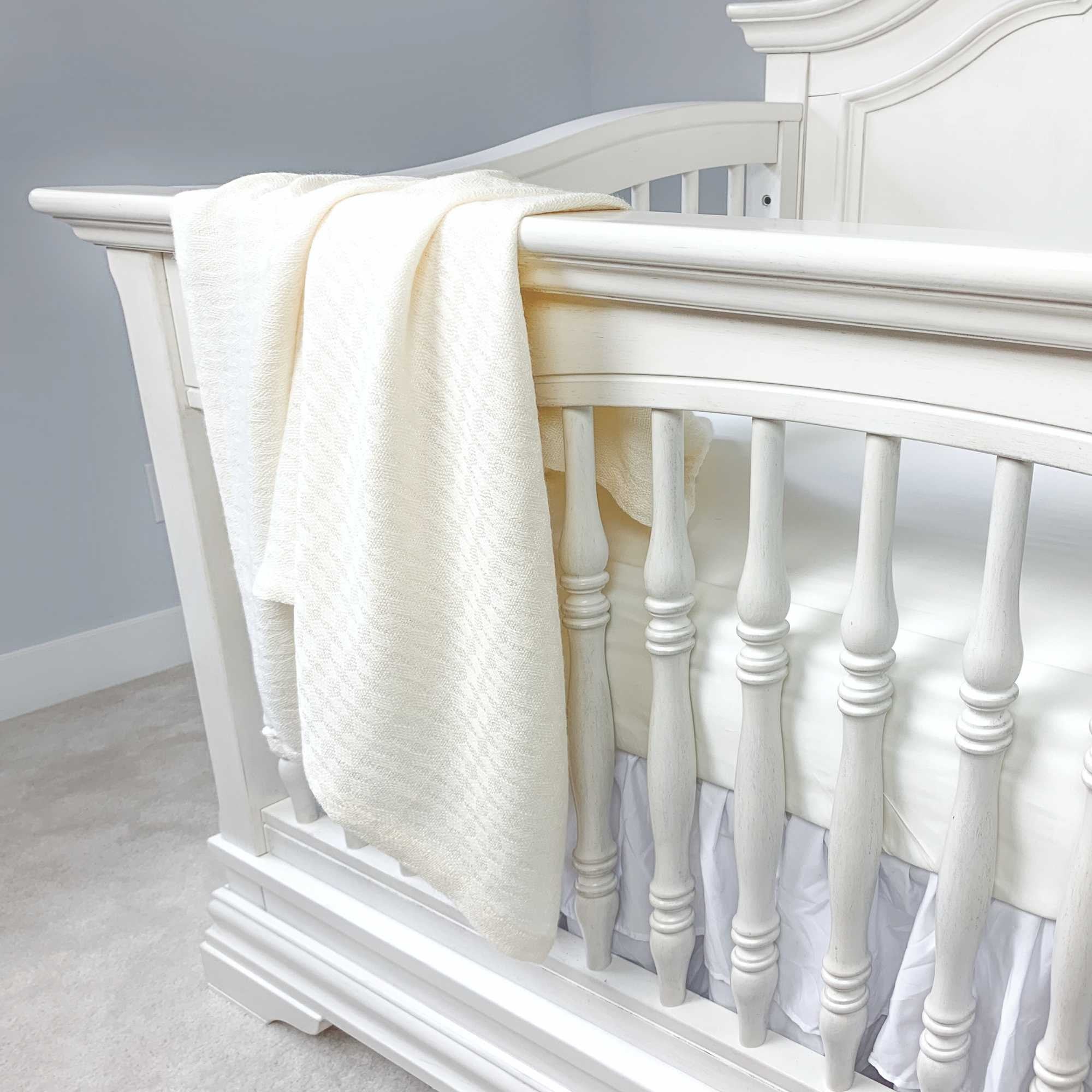 ivory bamboo blanket hanging over a crib with an ivory fitted sheet on mattress 