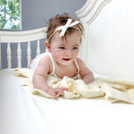 cute baby girl laying in crib smiling on ivory bamboo crib sheet and blanket