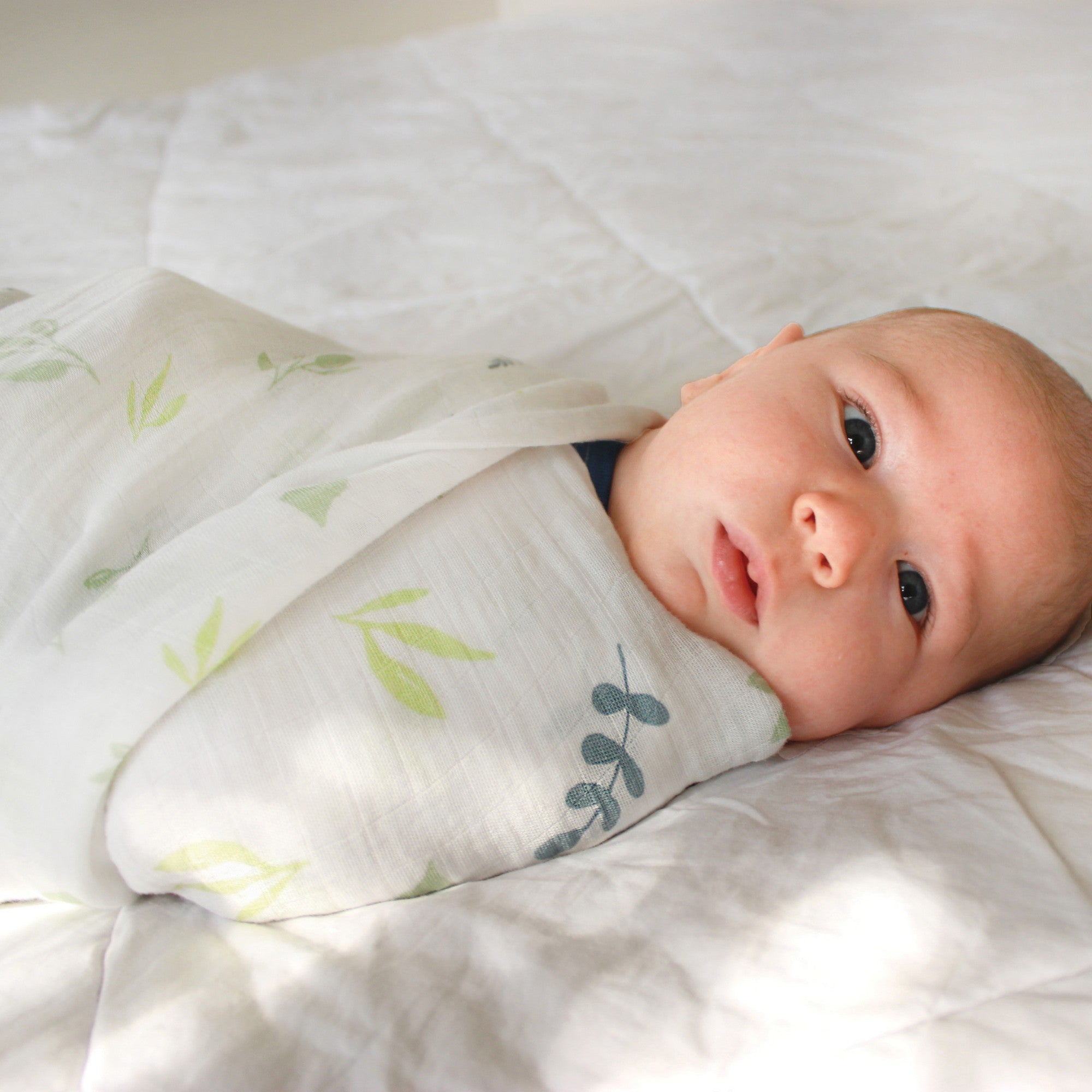 baby wrapped in bamboo muslin swaddle with green leaves on fabric