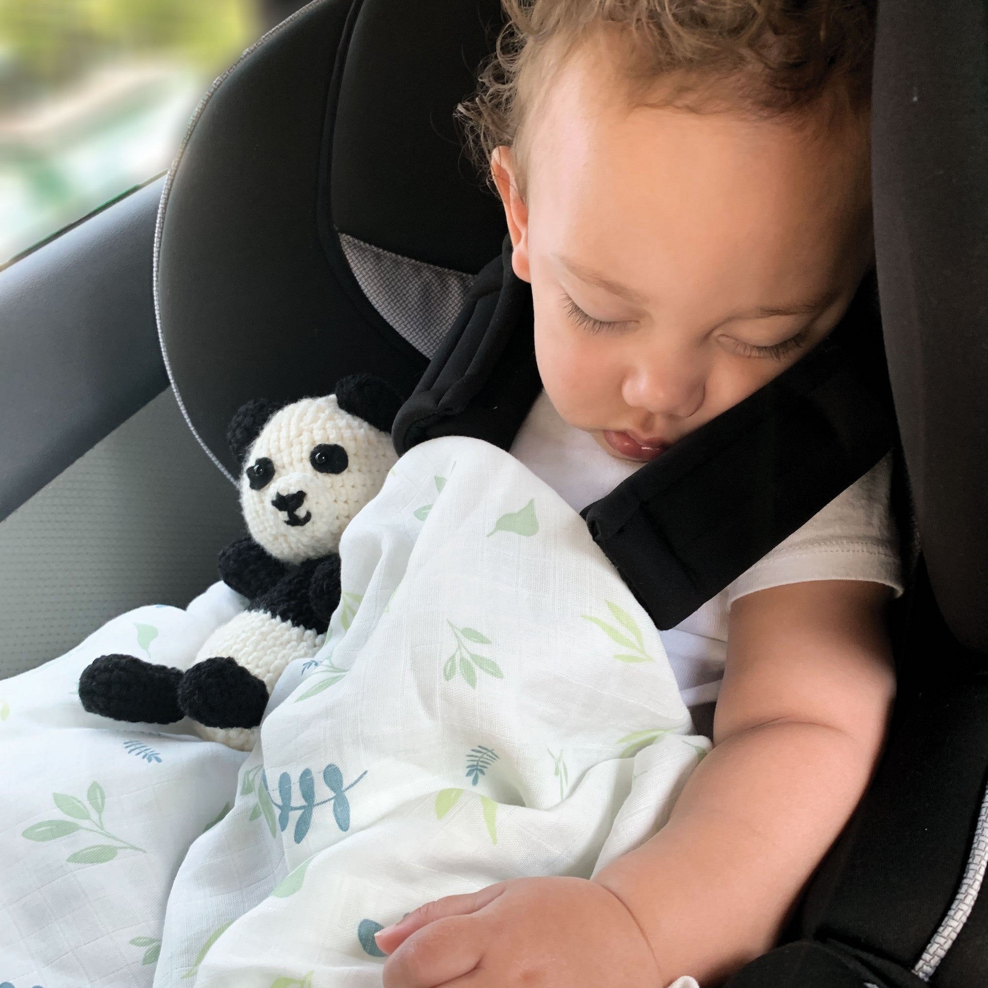 baby boy in car seat sleeping holding a panda doll and a bamboo leaf printed swaddle blanket
