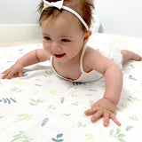 little baby girl smiling while playing on a bamboo muslin swaddle with leaf print