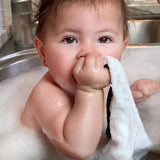 baby girl in sink taking a bath and chewing on a bamboo washcloth