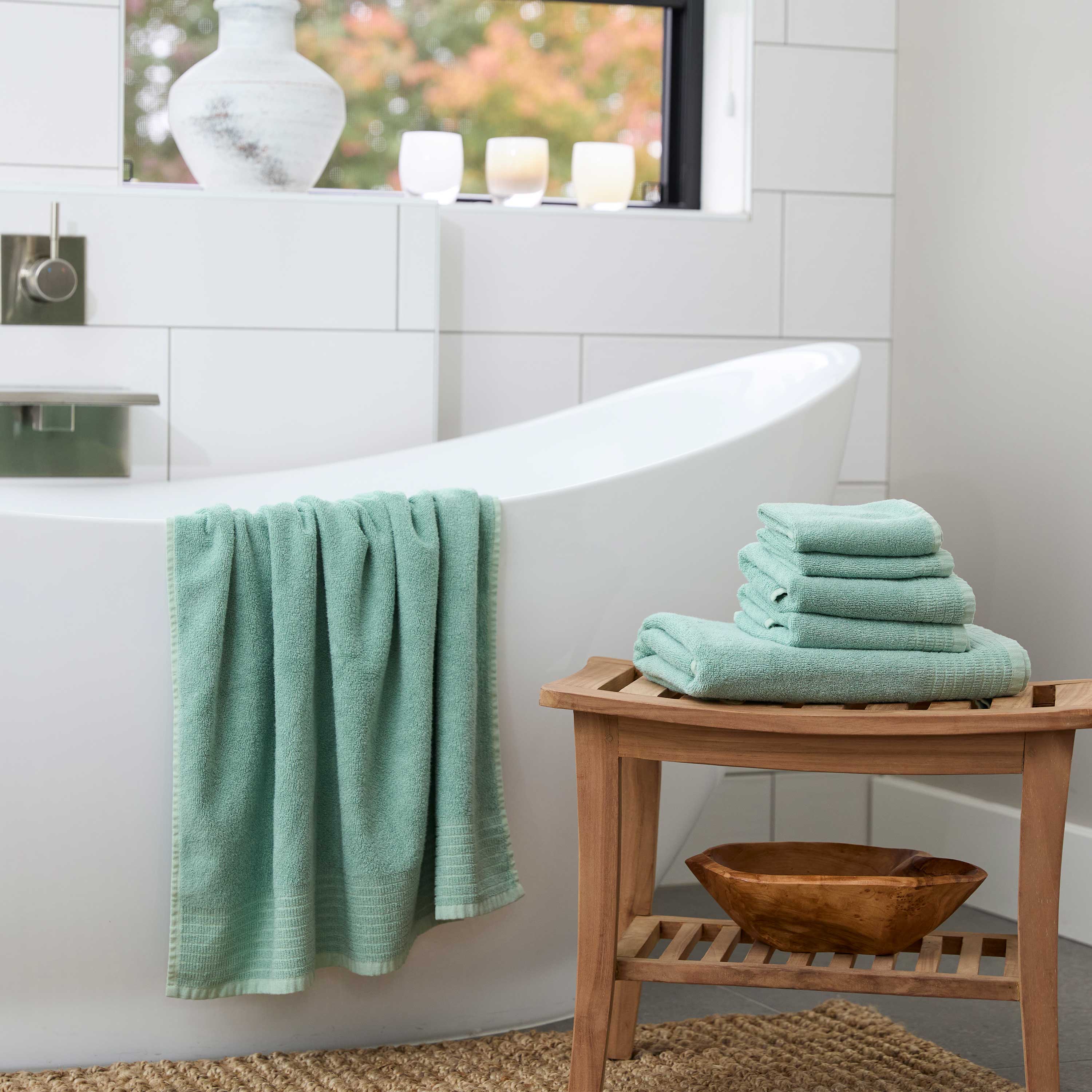 Seaglass green bamboo towel set, draped over a bathrub and stacked on a bamboo stool in beautiful bathroom