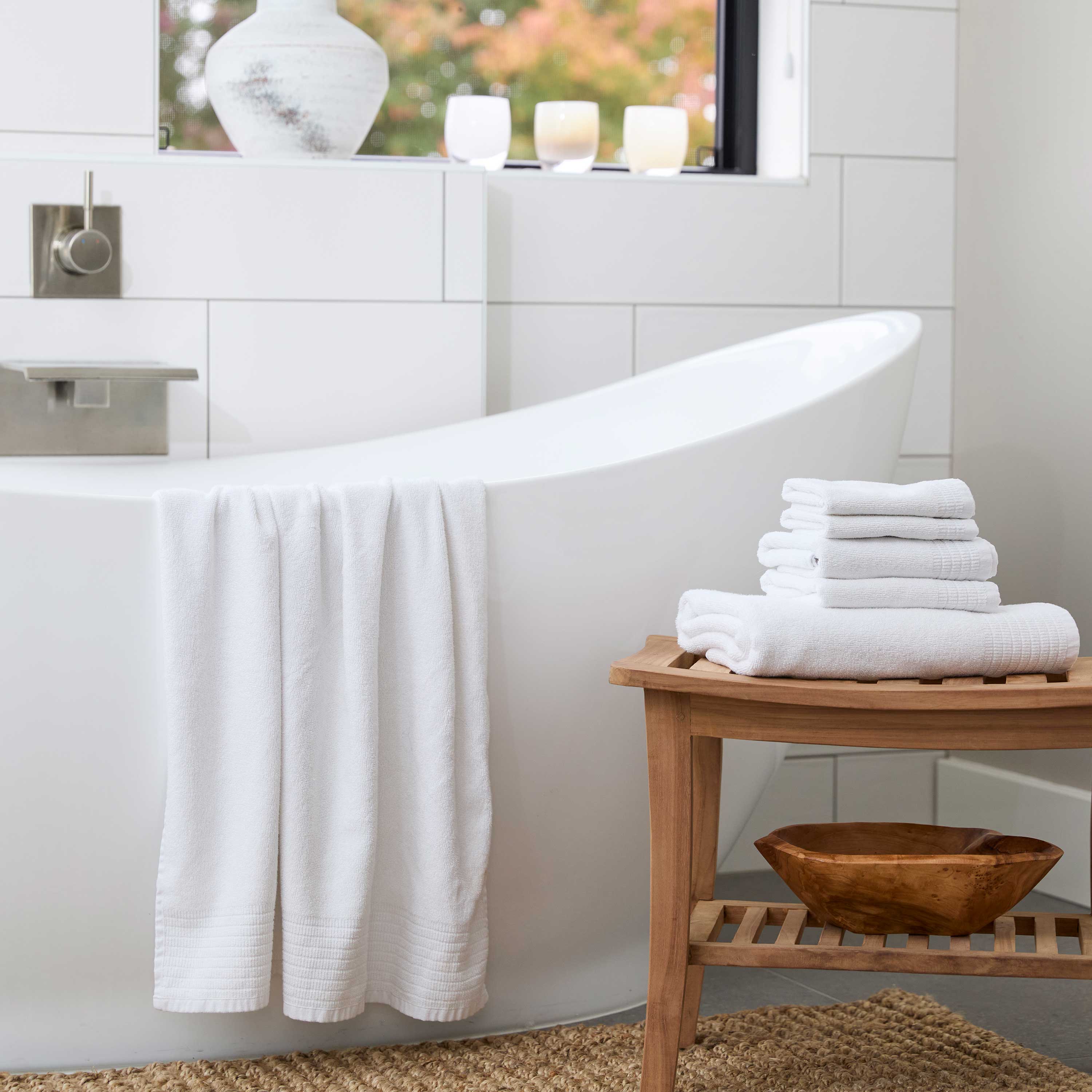 White bamboo towel set, draped over a beautiful tub, with 6pc towel set stacked on a bamboo stool in gorgeous bathroom