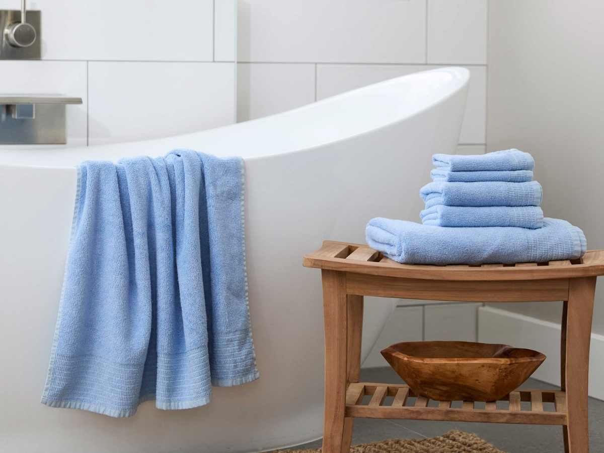 ocean blue bamboo towel draped over a white bathtub with stack of blue towels on bamboo stool